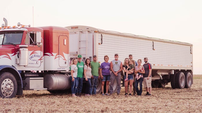 A multigenerational family stands in front of a semi smiling A multigenerational family stands in front of a semi smiling