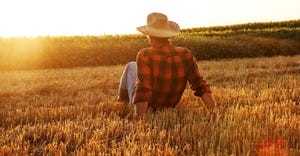 A farmer sits in a harvested wheat field watching the sun set
