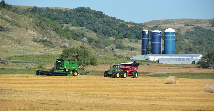 combine, tractor and wagon in field, silos behind