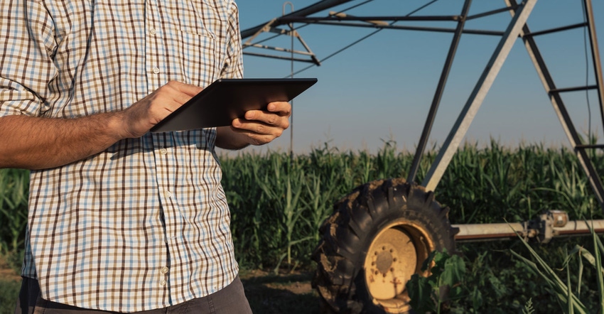 Close up of farmer using a tablet in a field with irrigation system behind him
