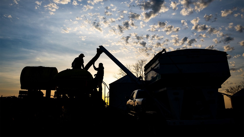 A silhouette of farmers working on a tractor with a sunset in the background