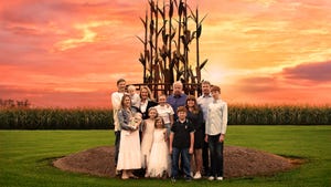 A mulitgenerational family pose in front of a sculpture and cornfield against a colorful sky
