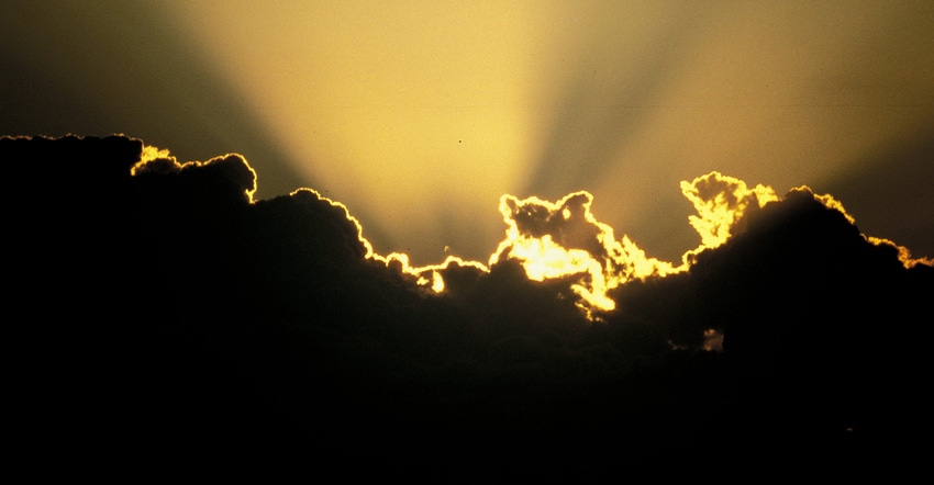 Sun setting behind a silhouette of clouds casting sun rays in the sky