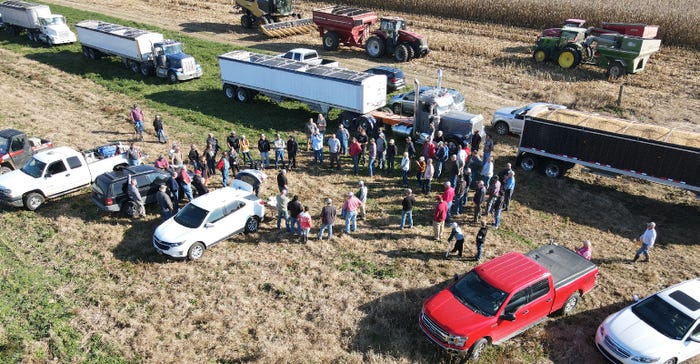 aerial photo of group of people gathered in field amid tractors, grain trucks and other vehicles