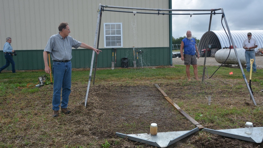 A man pointing towards a rainwater demonstration showing cover crops vs. bare soil