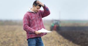 worried man standing in field and looking at papers tractor in background