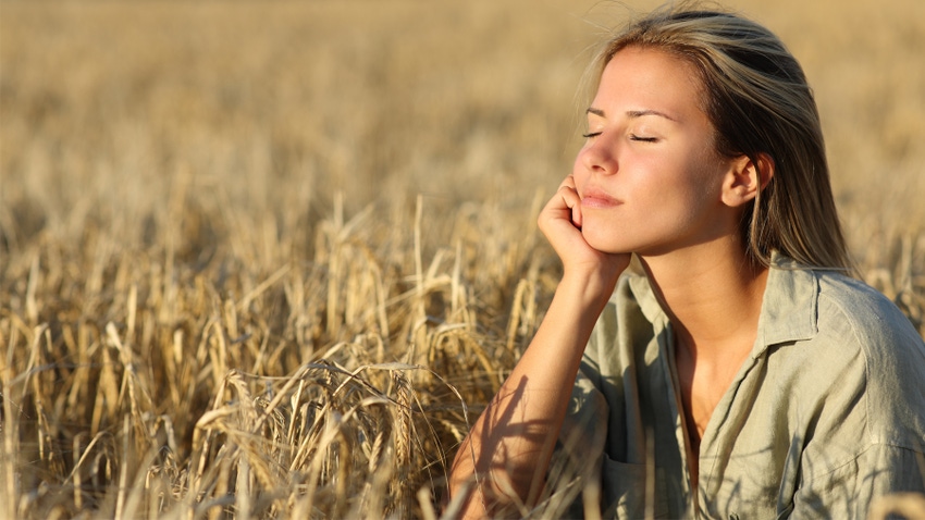 Woman sitting in wheat field with closed eyes