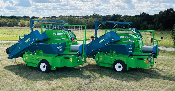 Two green and blue machines that hold feed displayed on a field