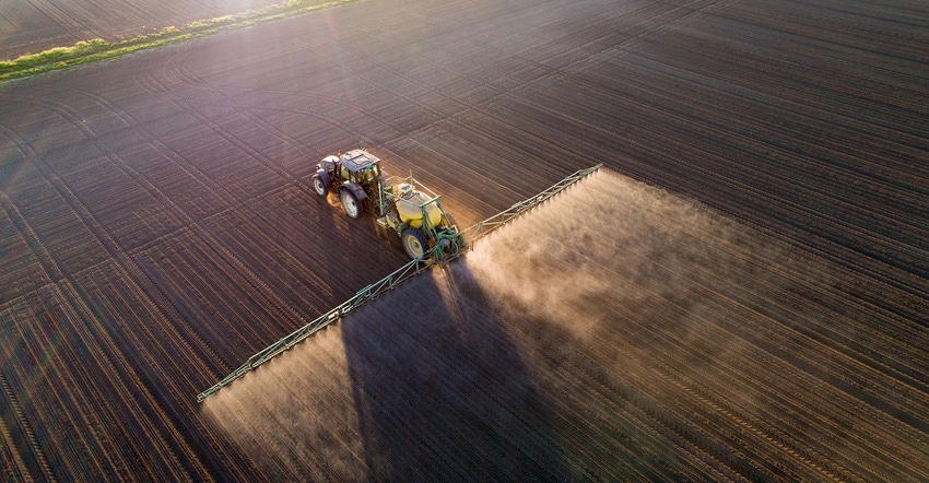 Aerial view of tractor applying fertilizer, spraying chemicals on field in spring.