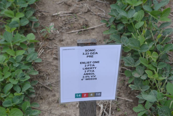 Rows of soybeans and a white sign on a wooden post
