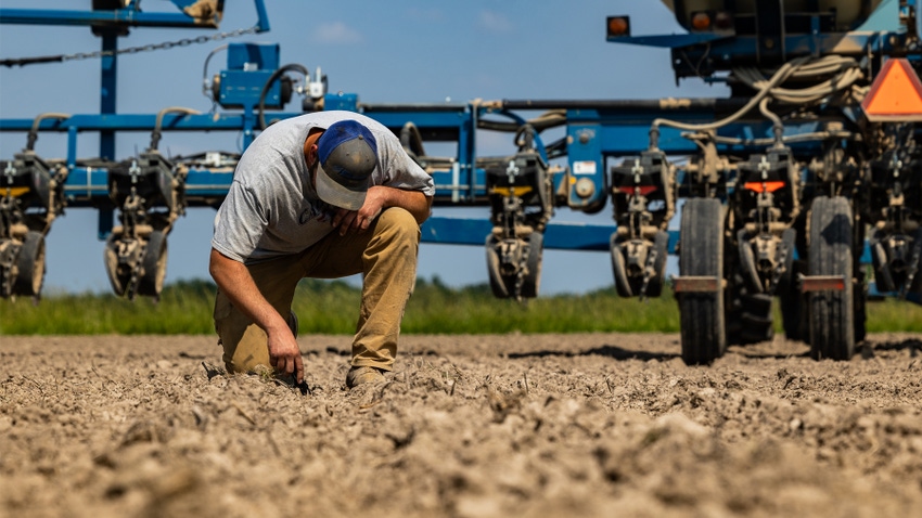 Farmer in field checking soil with planter in background