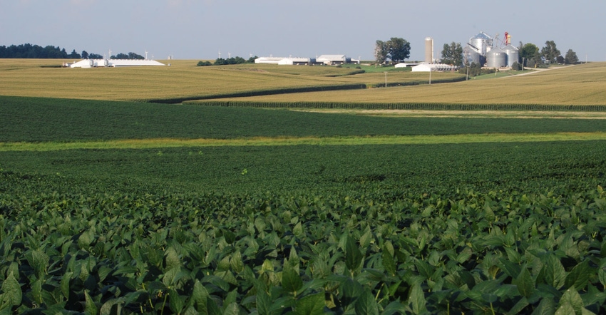 Landscape view of corn and soybean fields with farm buildings on horizon