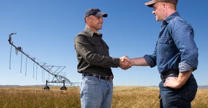two farmers shaking hands with irrigation equipment in background