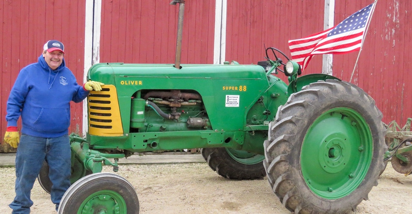 A man in a blue sweatshirt leaning against a green tractor with an American flag attached to it