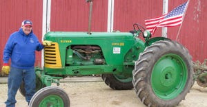 A man in a blue sweatshirt leaning against a green tractor with an American flag attached to it