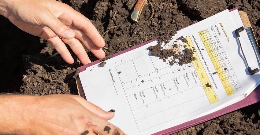 hands and clipboard, examining soil's organic matter