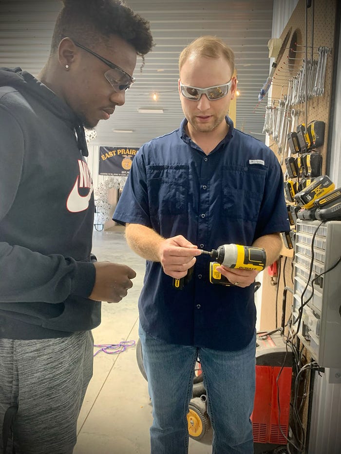 A teacher showing a student how to use a drill