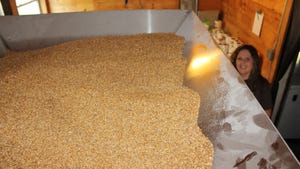 A large metal container filled with wheat berries and a woman smiling in the background