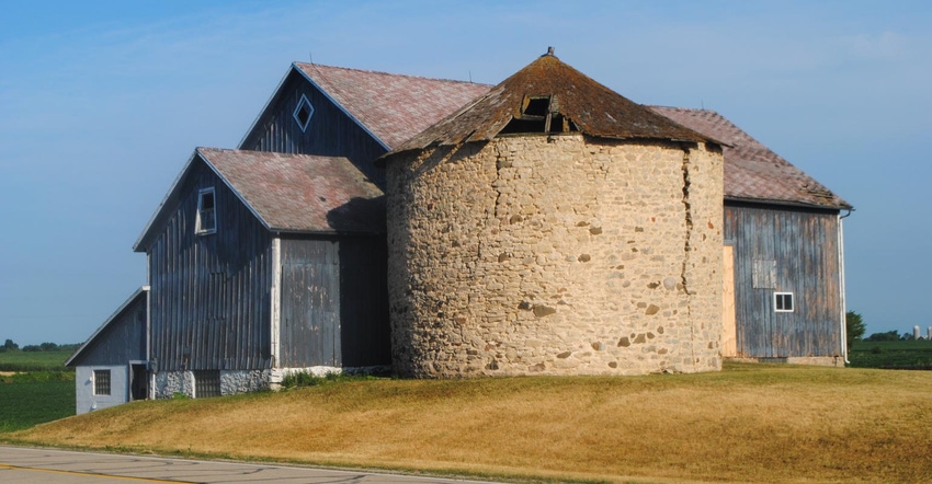 A barn next to a stone grain bin with a damaged roof