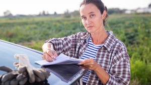 Female farmer signing papers near car in farm field