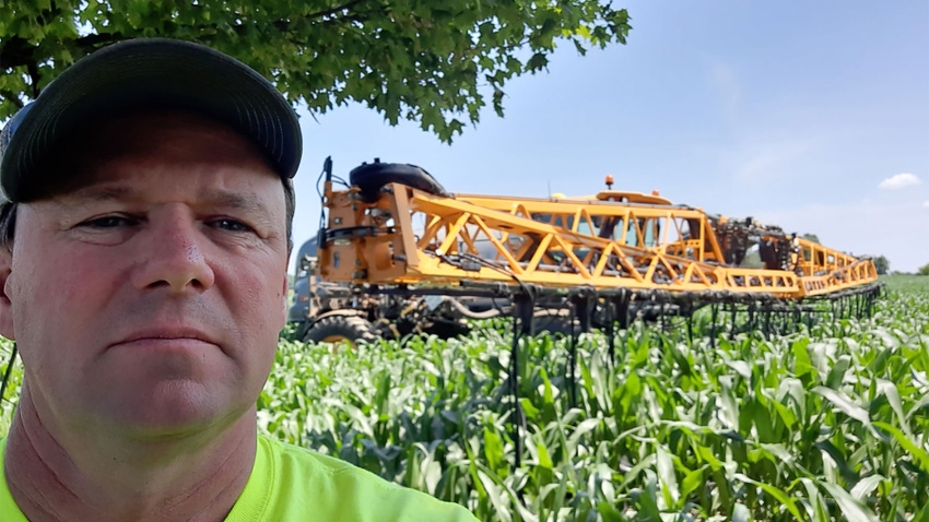 A farmer with a sprayer in a field of crops in the background