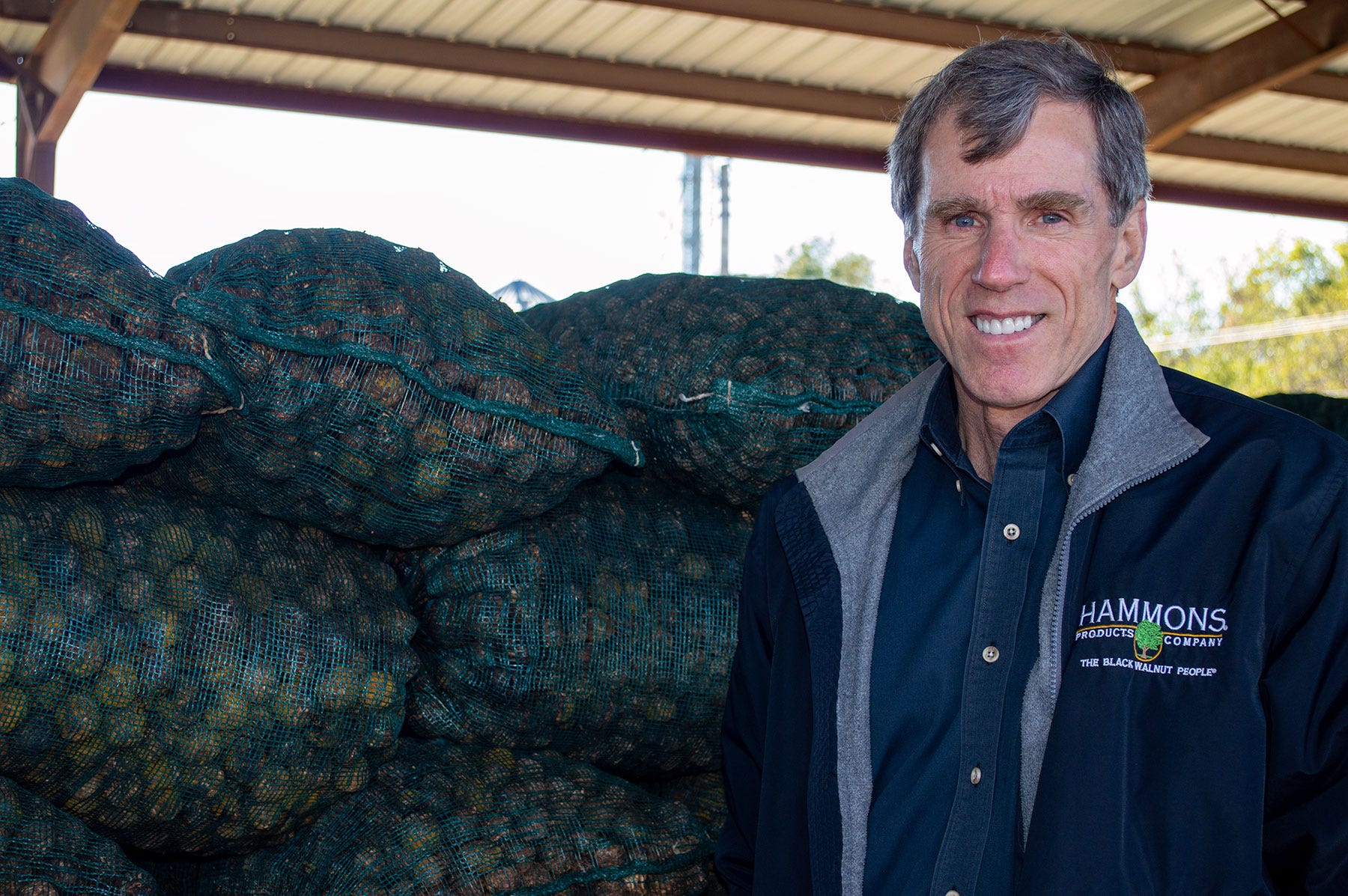 Joann Pipkin - Brian Hammons smiling with bags of walnuts stacked behind him