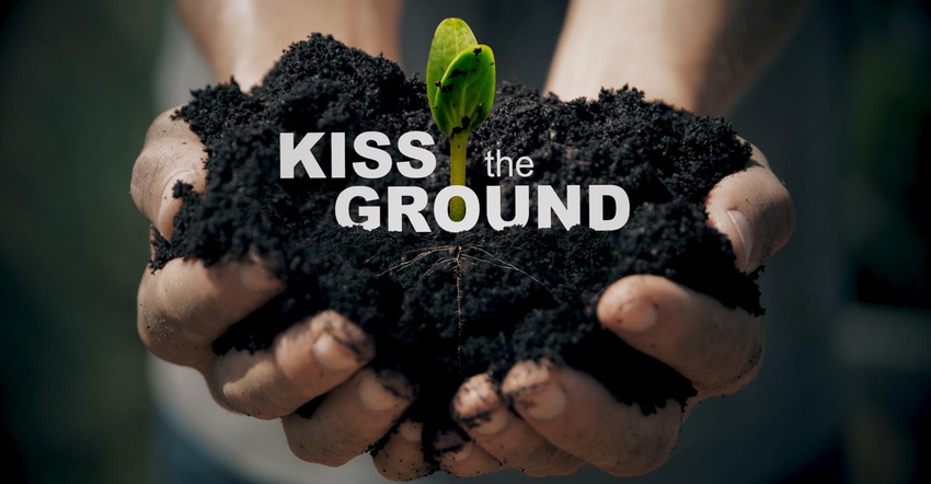 Hands holding a mound of soil with a plant sprouting and the words Kiss the Ground over top of the soil