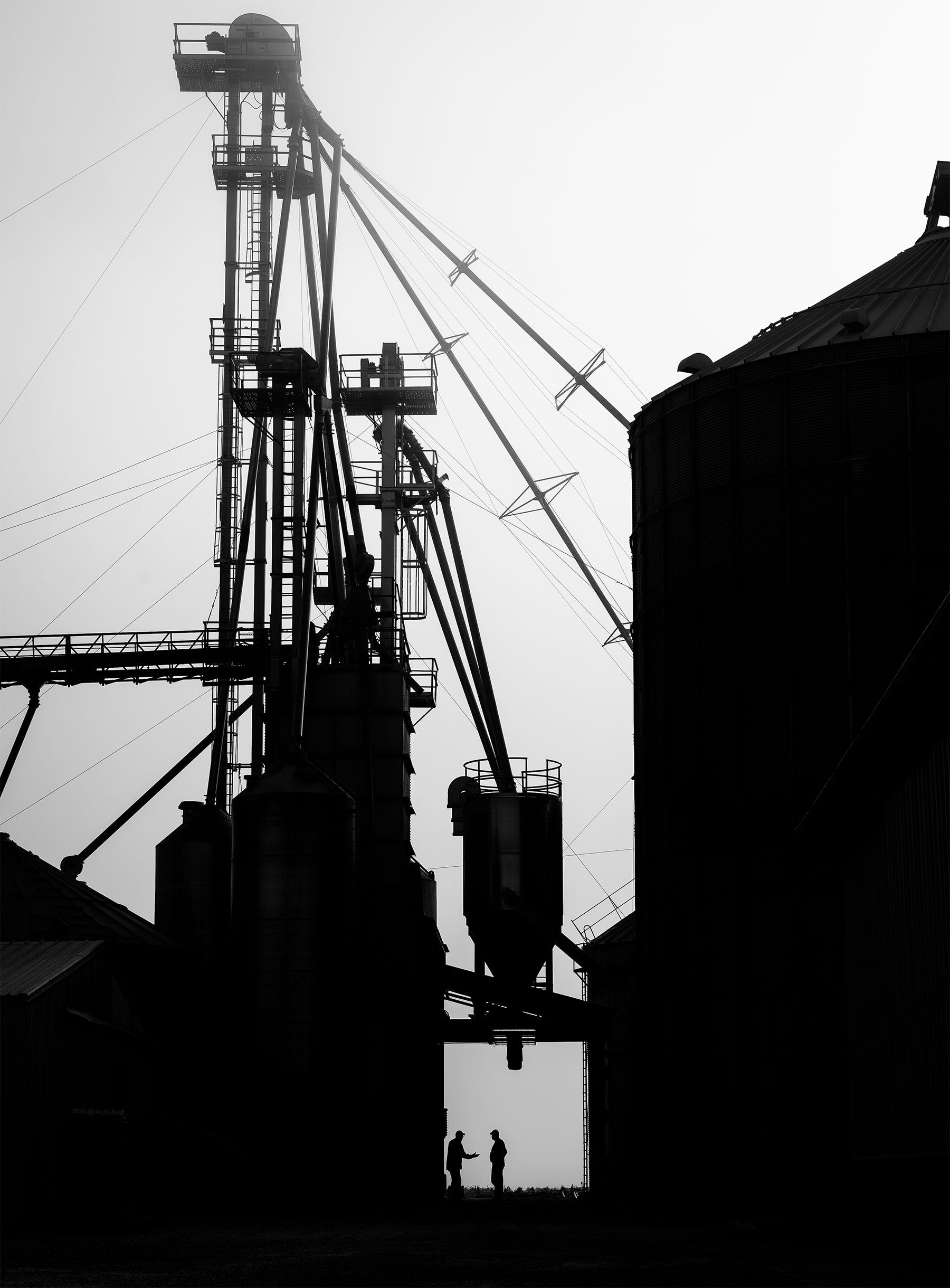 silhouette of two farmers talking beneath a large grain setup