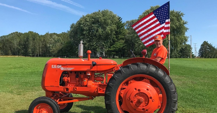 A man sitting on a tractor next to an American Flag in an open field