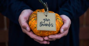 Male hands holding a pumpkin with a "give thanks" tag hanging from the stem