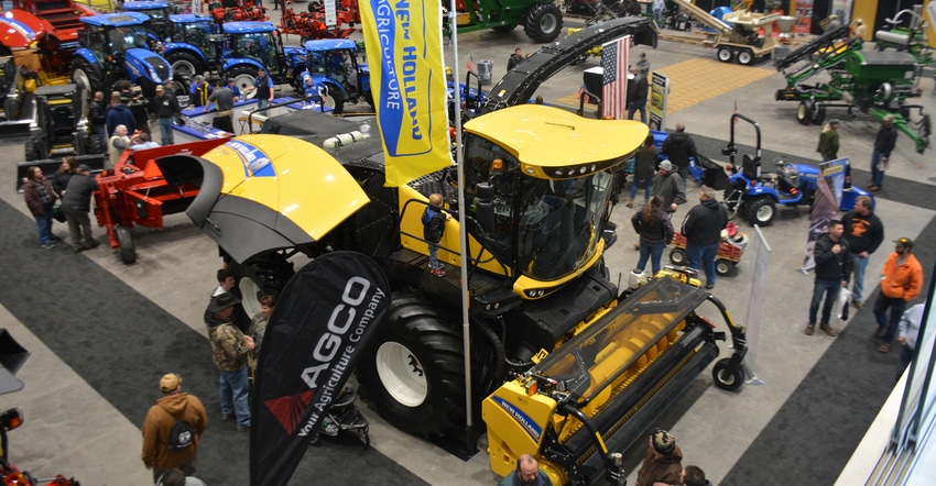 A yellow tractor showcased at an exhibition surrounded by spectators A yellow tractor showcased at an exhibition surrounded by spectators