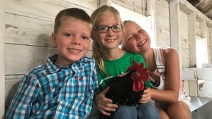 Three young children holding rooster