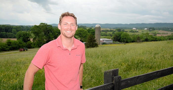 Man standing against fence with farm landscape in background.