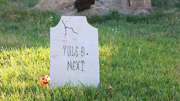 A hand made tombstone with the words Yule B. Next and a small plastic pumpkin