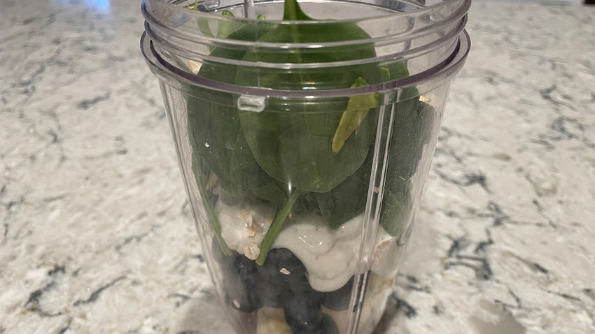 A clear blender cup with spinach, yogurt and fruit