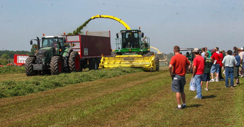 A crowd of people gathered to watch a tractor at work, in a field A crowd of people gathered to watch a tractor at work, in a field