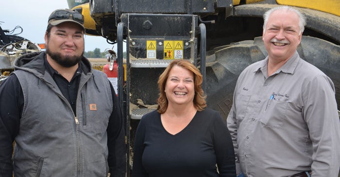 Three farmers smiling in front of implement