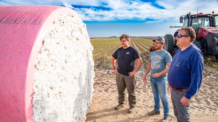 Three farmers standing next to bale of cotton