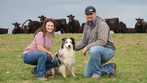 a young couple with their Australian shepherd and a herd of cattle behind them