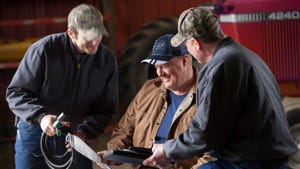 3 farmers look over tablet and paperwork in barn