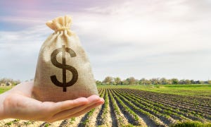 Hand holding sack of money in front of a farm field.