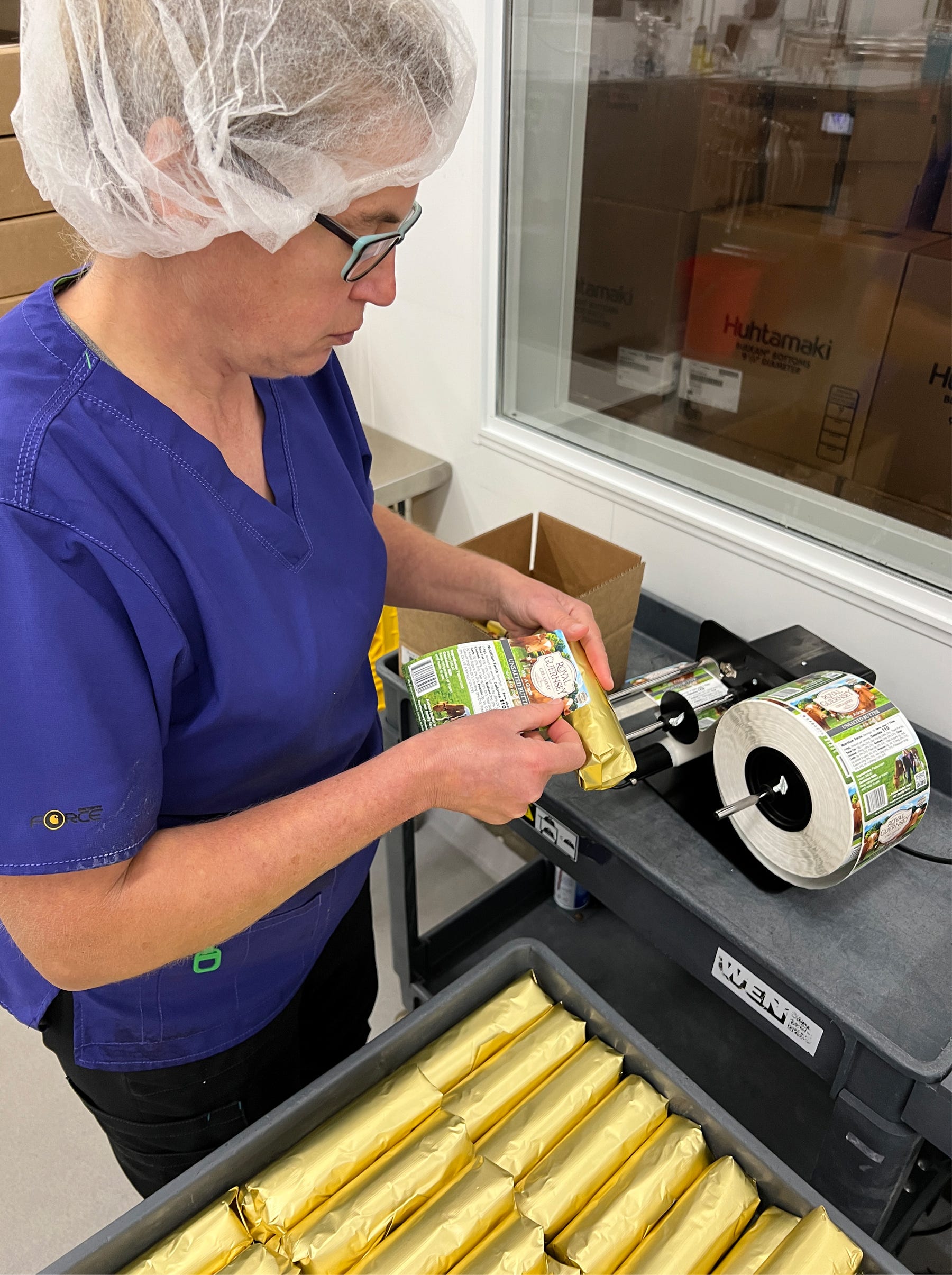 a woman applies a Royal Guernsey Creamery label to a golden-wrapped roll of butter