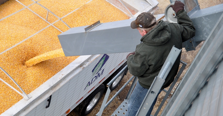 aerial view of man watching corn pour from bin auger into ADM truck 