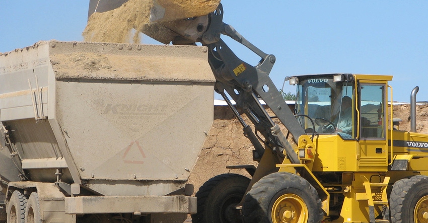 Digger truck shoveling feed into truck cargo bed Digger truck shoveling feed into truck cargo bed