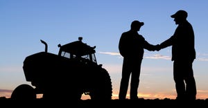 silhouettes of farmers shaking hands in front of a tractor at sundown