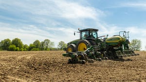 Green tractor pulling planter to plant corn field