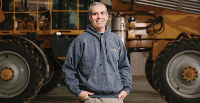 White man standing by sprayer in a shed.