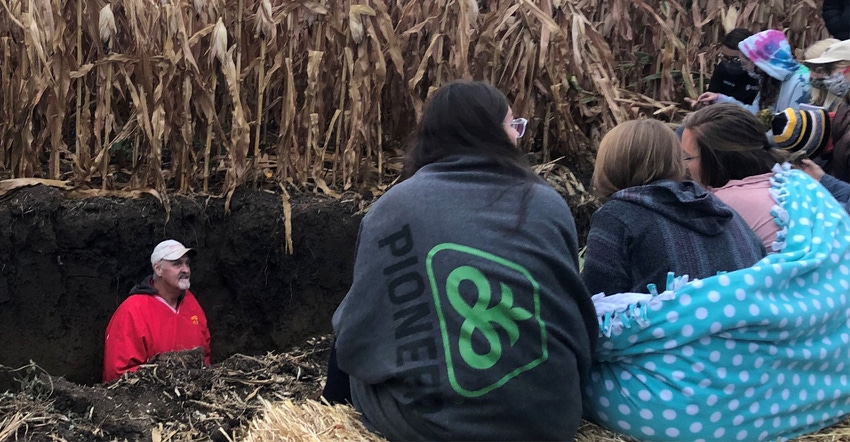 An instructor digging pit in field to examine root depth while students watch.