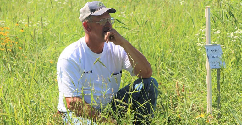 Montgomery County farmer Harry Cope kneels in native grass