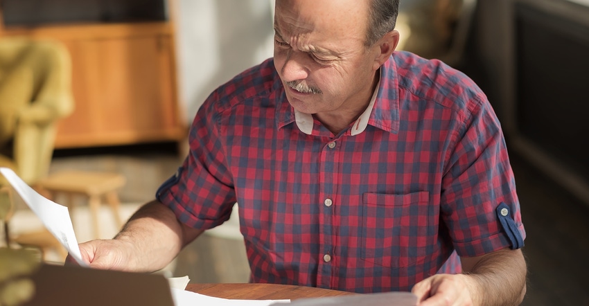 Man evaluating a piece of paper on a desk in concentration.